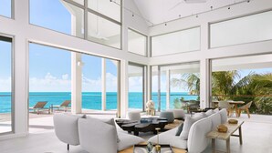 A spacious living area with a large window overlooking the sea, furnished with white sofas, a coffee table, and a wooden bench.
