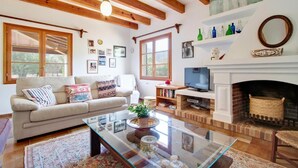 Ein gemütliches Wohnzimmer mit Sofa, Fernseher, Kamin und Holzbalken.