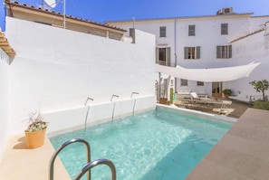 A swimming pool with a white wall and a shaded area. - Casa Campomar by Vida Villas (Pollença)