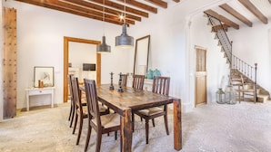 A dining area with a wooden table and chairs, hanging pendant lights, and a staircase with wooden railings. - Casa Campomar by Vida Villas (Pollença)