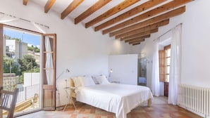 A bedroom with a large bed, wooden beams, a radiator, and a view of the outside. - Casa Campomar by Vida Villas (Pollença)