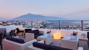 Une terrasse sur le toit avec des sièges extérieurs, une vue sur le paysage urbain et une montagne en arrière-plan.