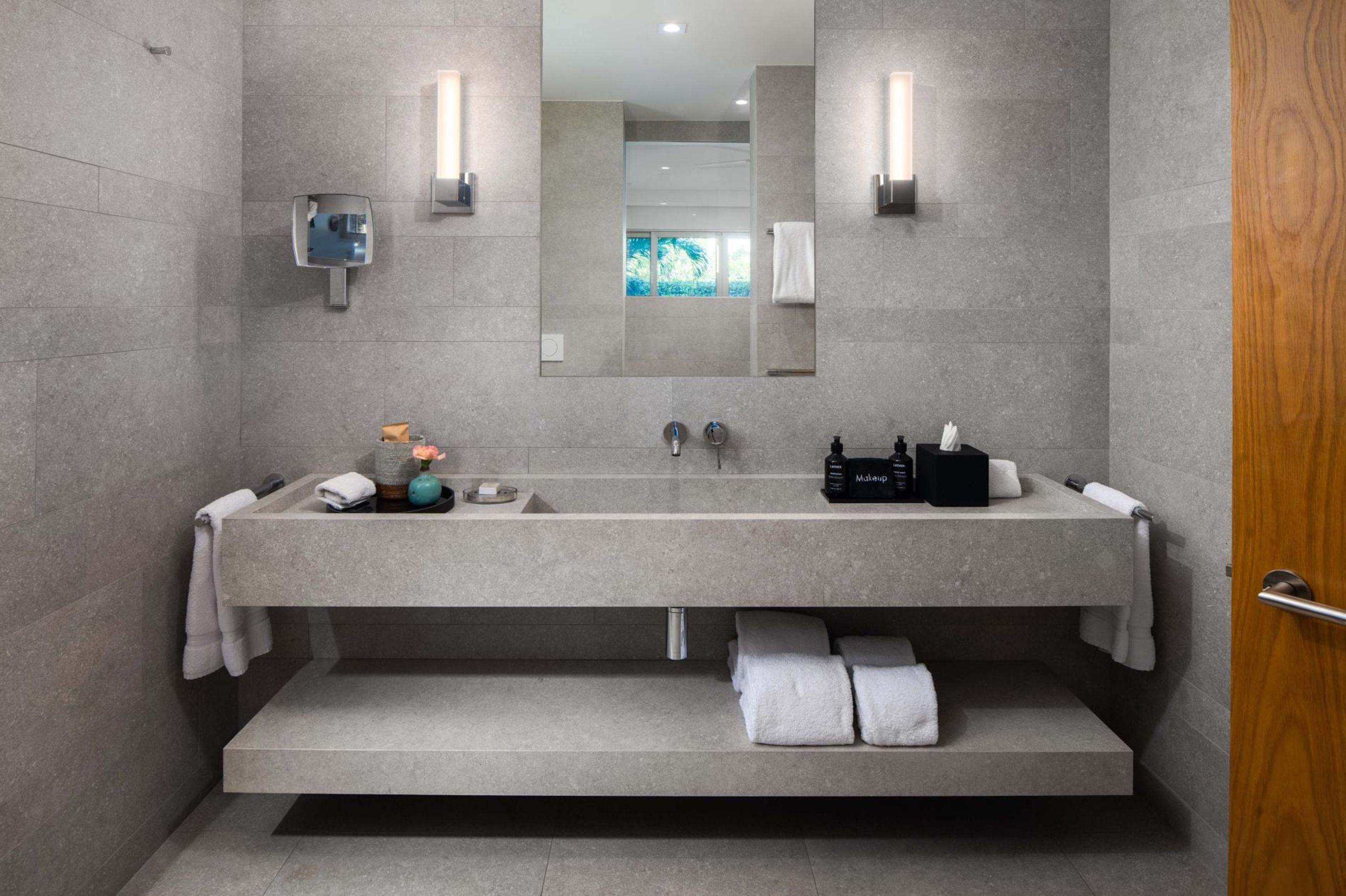 A modern bathroom with a large sink, two mirrors, a towel rack, and a small window.