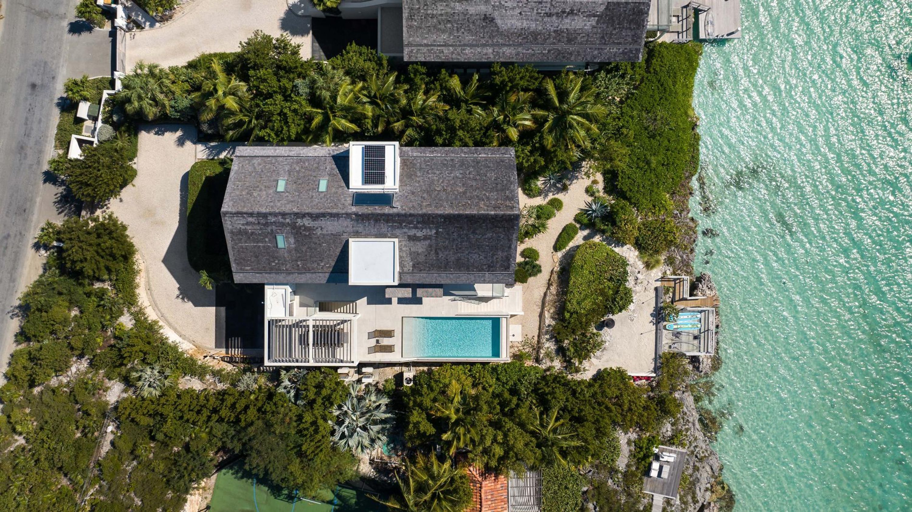 An aerial view of a coastal property with a swimming pool, a covered patio, and a beach area.