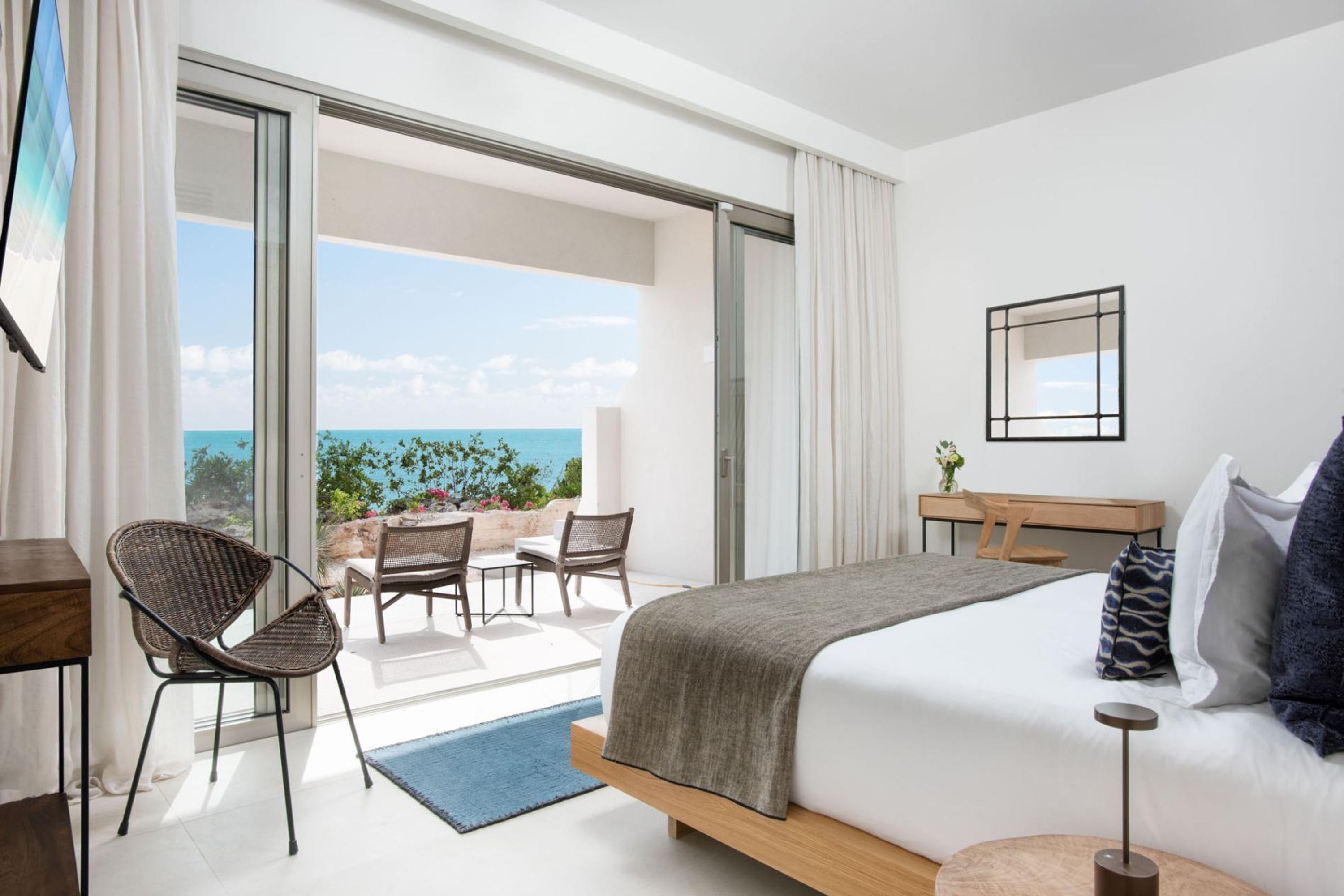 Ein modernes Hotelzimmer mit einem großen Bett, einem Schreibtisch und einem Balkon mit Meerblick.
