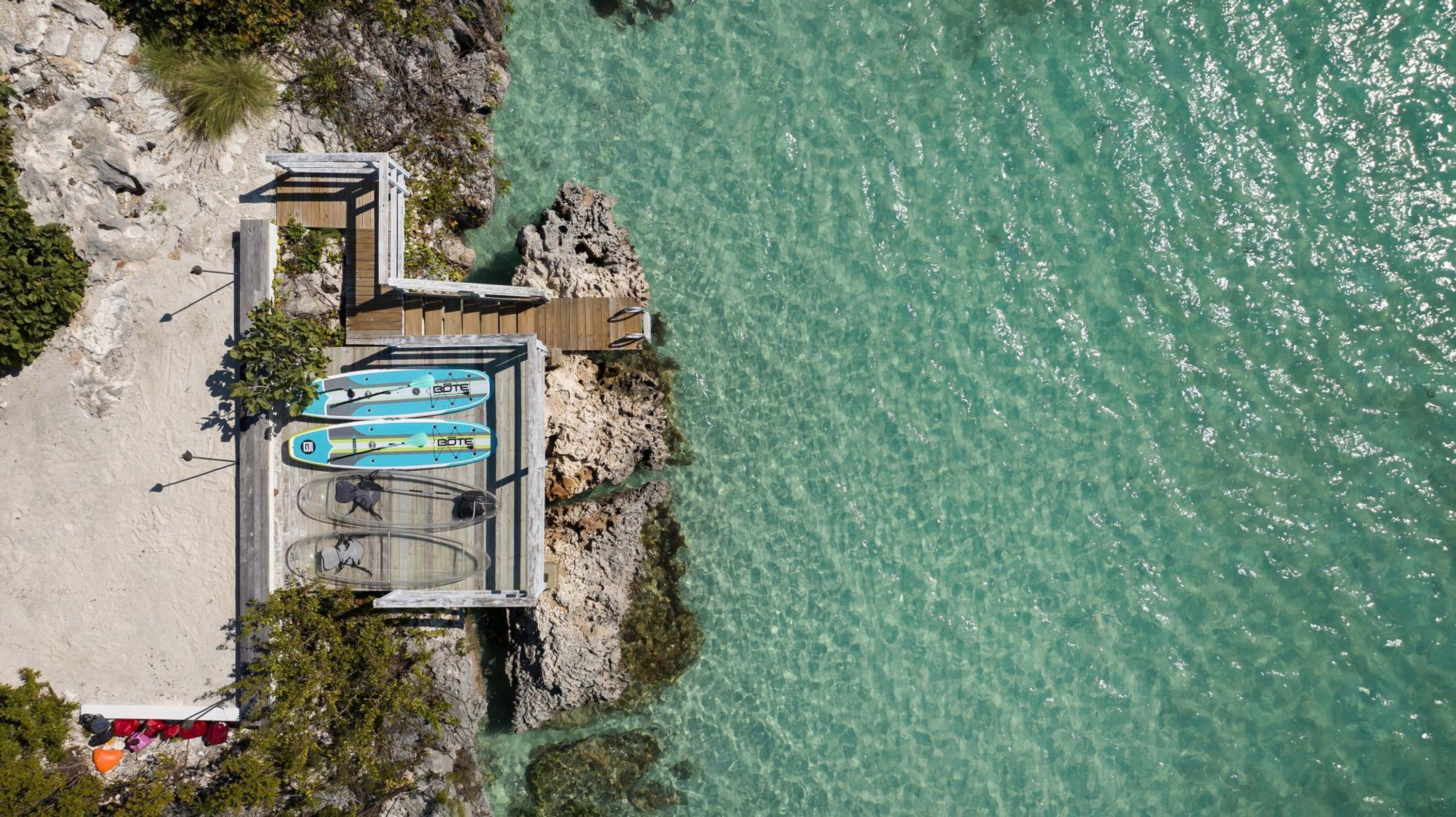 Eine Luftaufnahme einer Küstenregion mit einem hölzernen Steg, der sich in klares türkisblaues Wasser erstreckt.