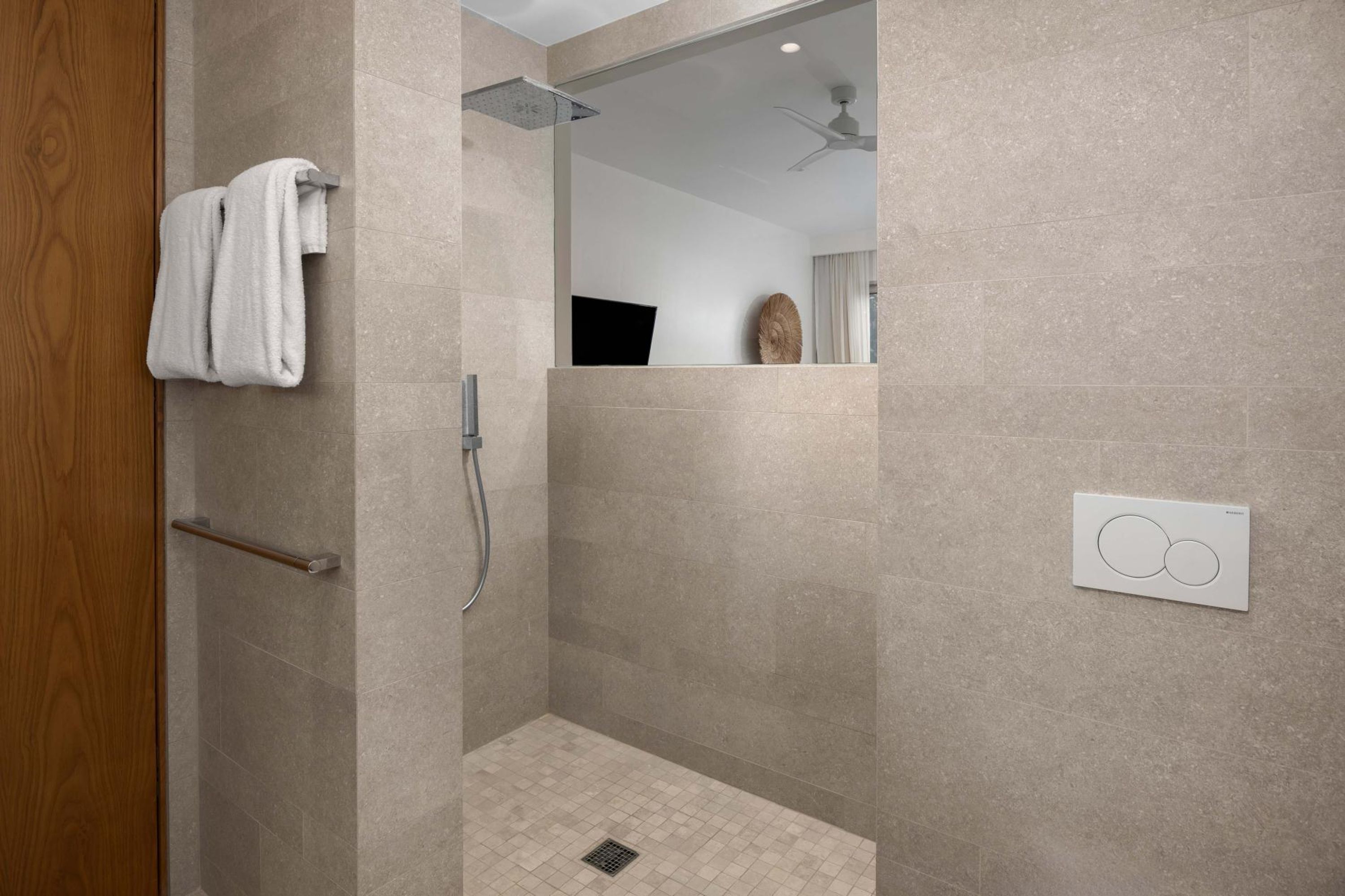 Une douche moderne équipée d’un pommeau de douche à main, d’un porte-serviettes et d’un panneau de commande mural.