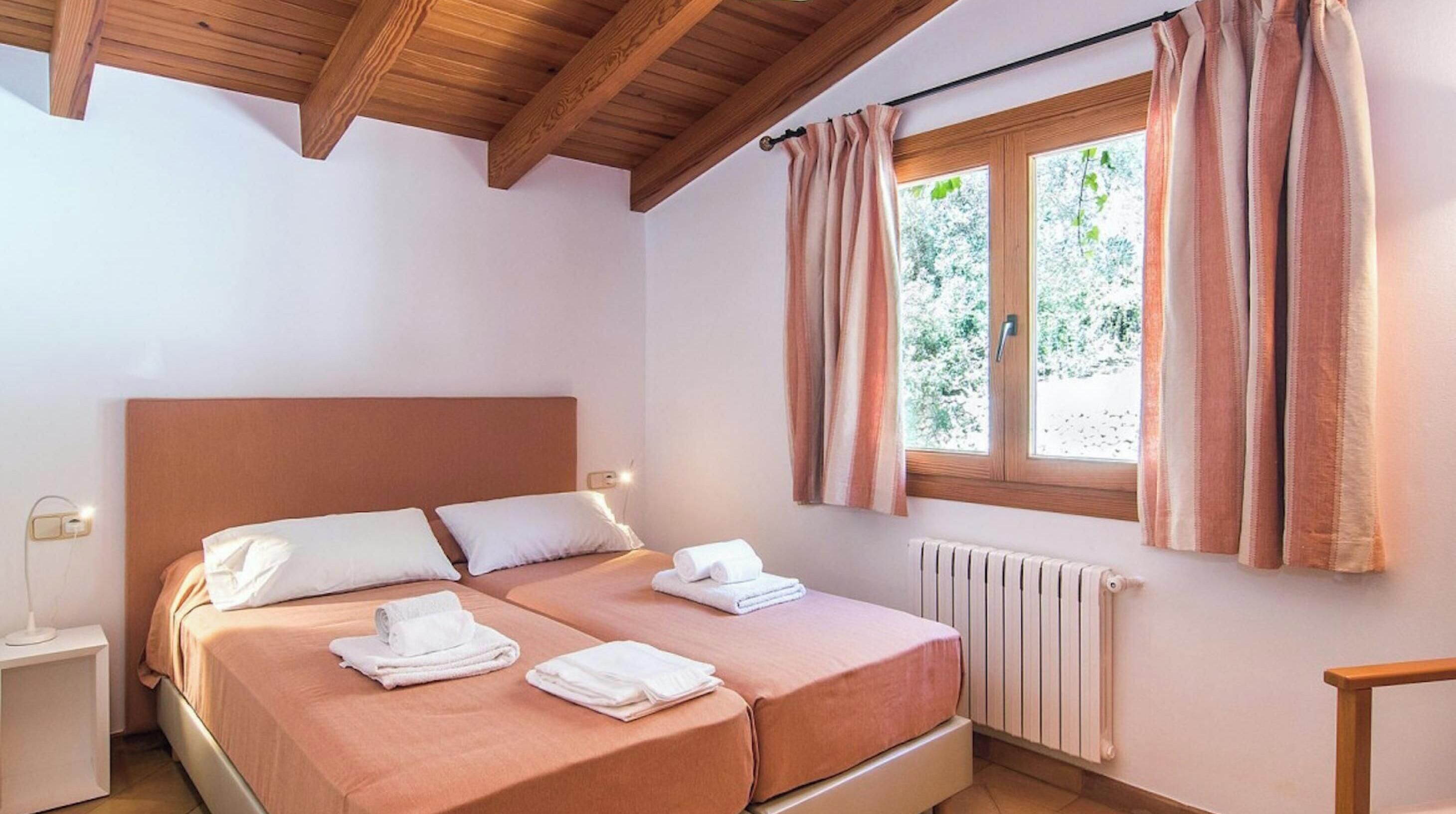 A double room with two beds, a wooden ceiling, a window with curtains, and a radiator.