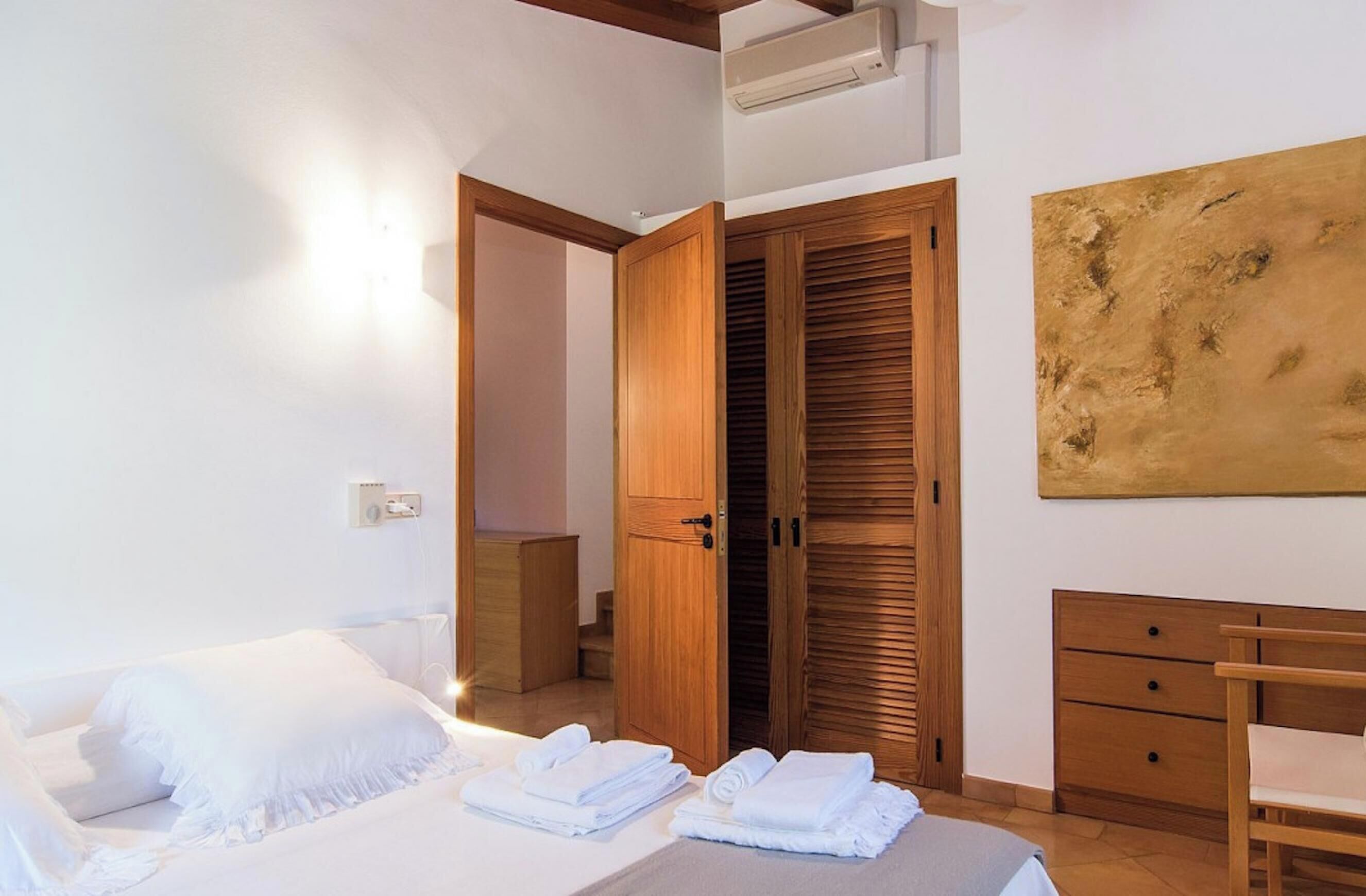Ein Schlafzimmer mit einem Bett, einem Holzschrank, einem Schreibtisch und einem großen abstrakten Gemälde.