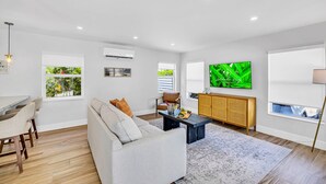 Ein modernes Wohnzimmer mit Sofa, Couchtisch, Essbereich und Fernseher an der Wand.