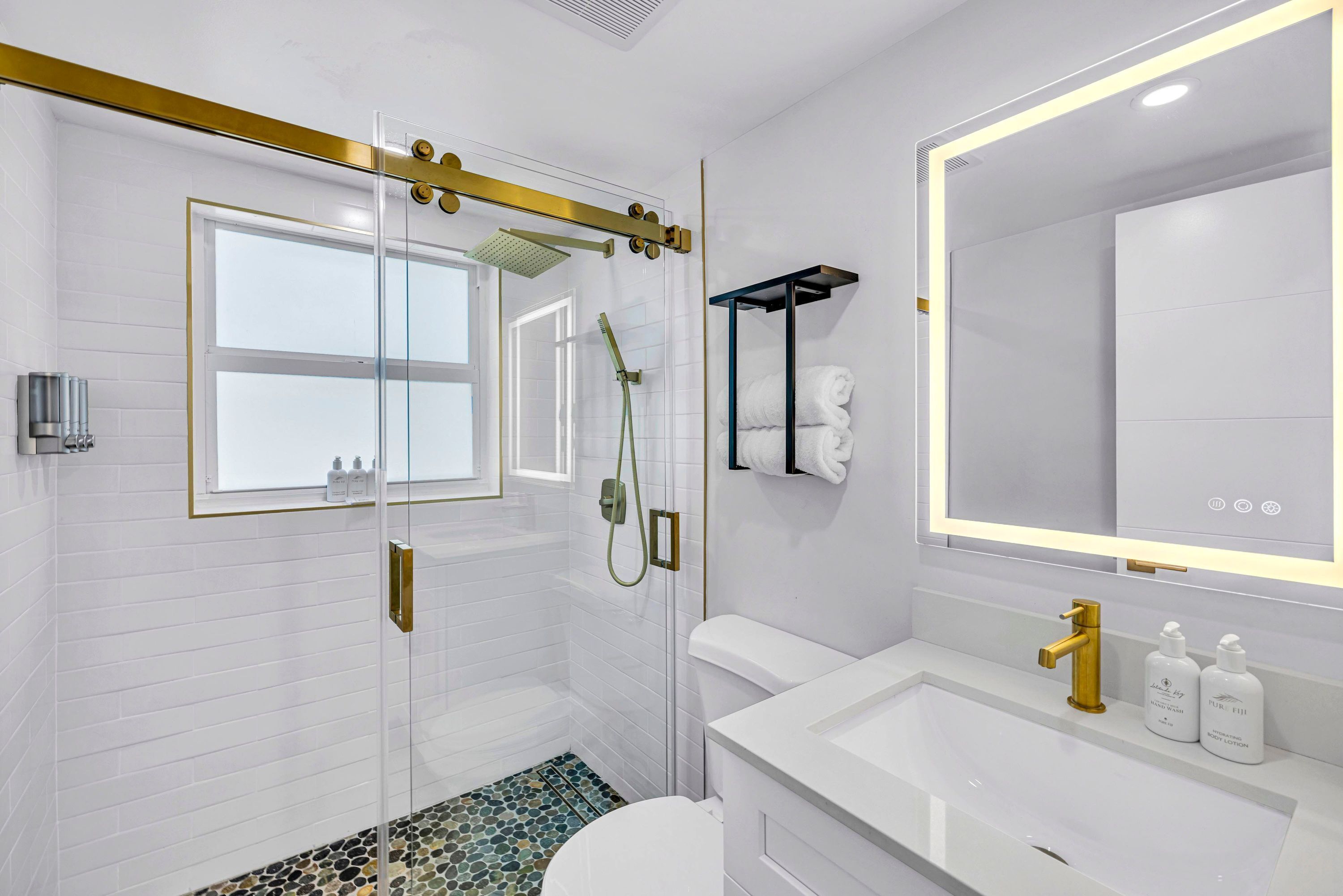 A modern bathroom with a glass-enclosed shower, a white sink with gold fixtures, and a large mirror.