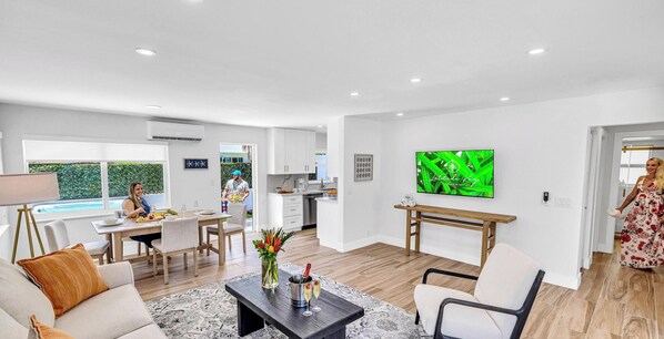 A modern living room with a sofa, coffee table, and TV. There's a dining area with a table and chairs, and a kitchen in the background. - Beach Condo King Bed Lush Patio w BBQ Birch Key Five (Fort Lauderdale)
