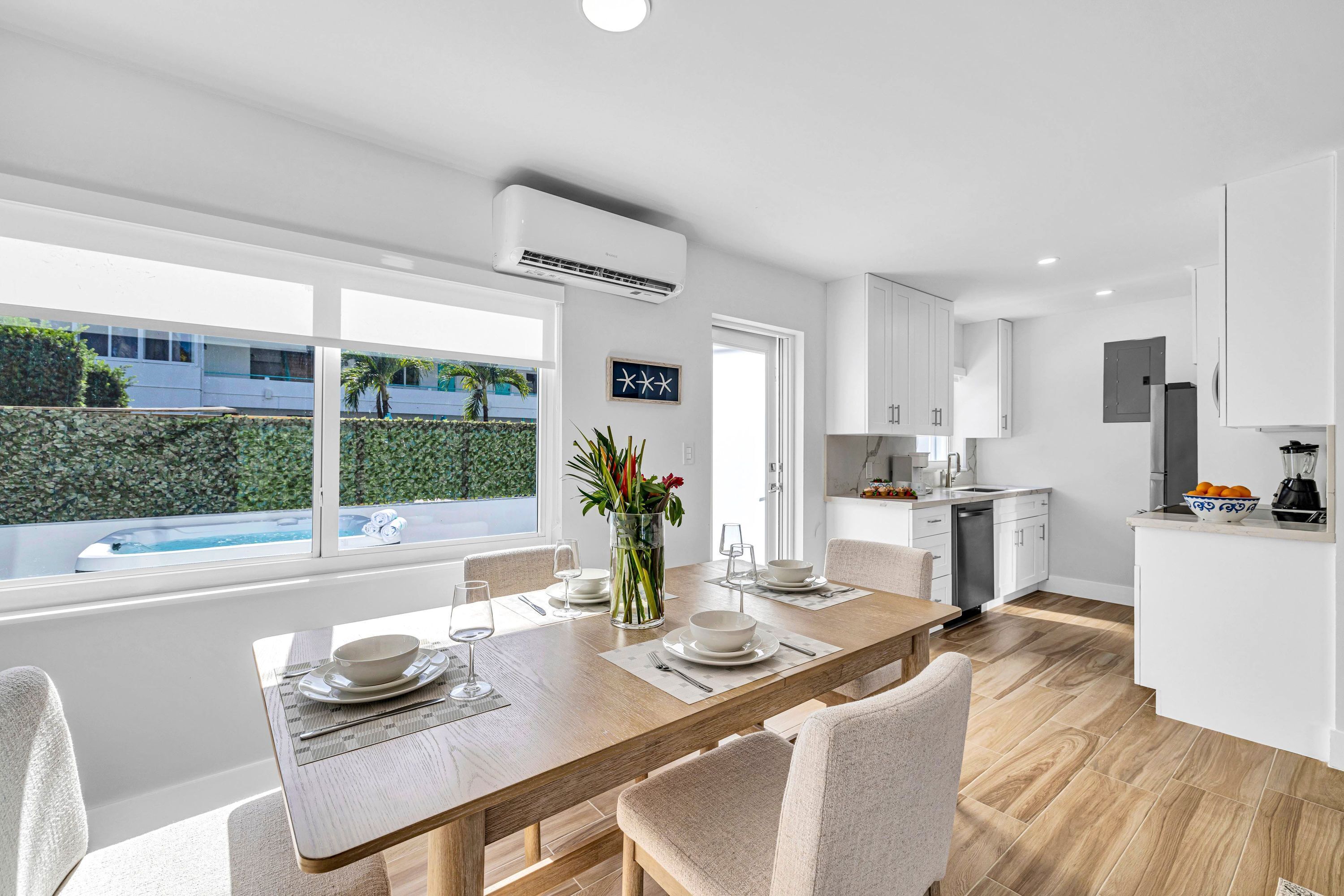 Una cocina moderna con armarios blancos, un comedor con mesa y sillas de madera, y vistas a una piscina exterior.