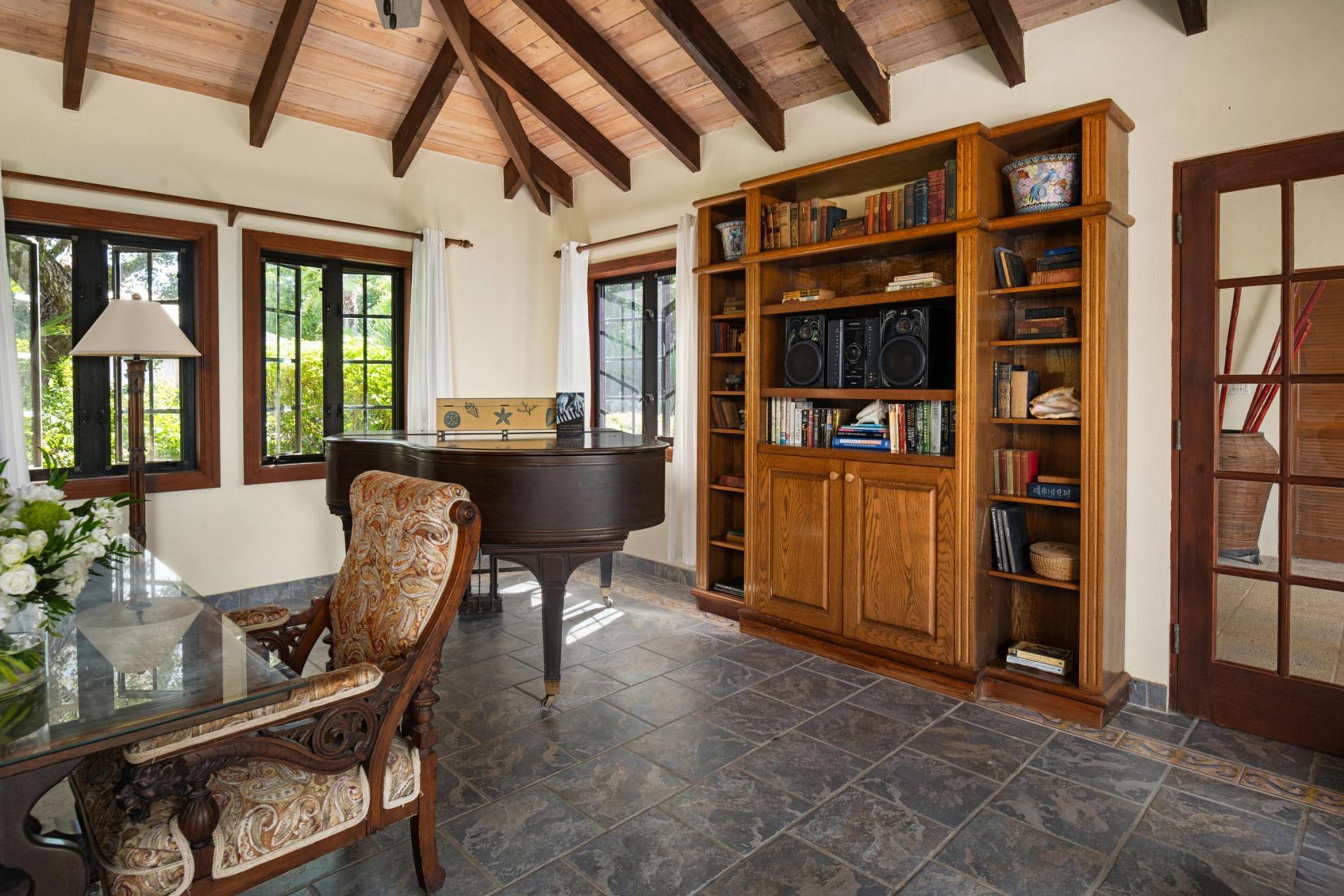 Una habitación con un piano, una amplia estantería de madera, una mesa de comedor con sillas y una mesa de vidrio con un florero.