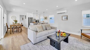A modern living room with a grey sofa, wooden dining table, and a coffee table with a fruit tray. - Beach Condo King Bed Lush Patio w BBQ Birch Key Eight (Fort Lauderdale)