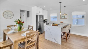 A modern kitchen with white cabinetry, a stainless steel refrigerator, and a marble island with bar seating. - Beach Condo King Bed Lush Patio w BBQ Birch Key Eight (Fort Lauderdale)
