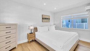 A bedroom with a bed, a nightstand, a dresser, a window with a view, and a painting on the wall. - Beach Condo King Bed Lush Patio w BBQ Birch Key Eight (Fort Lauderdale)