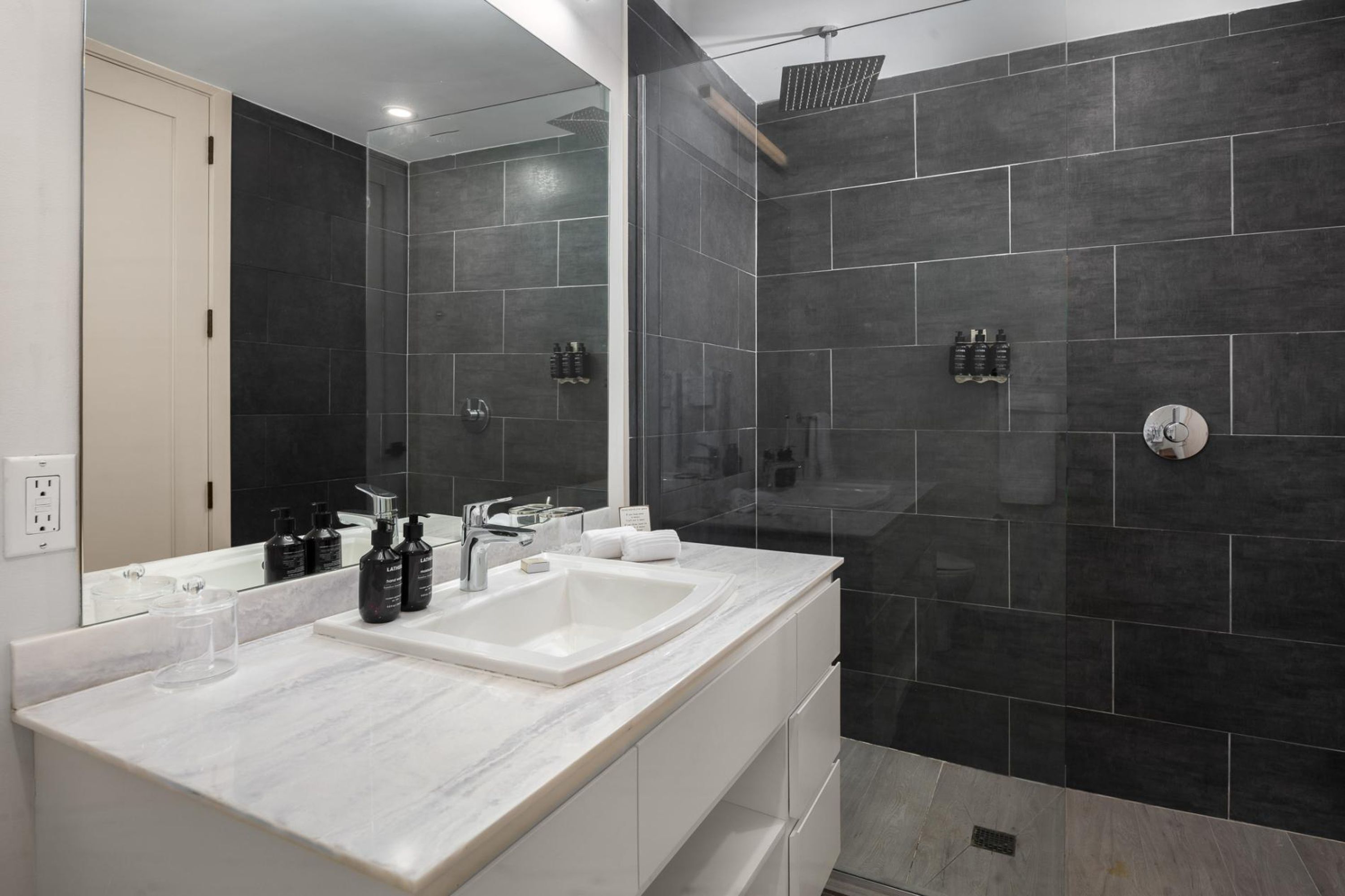 A modern bathroom with a large mirror, two sinks, and a shower area.