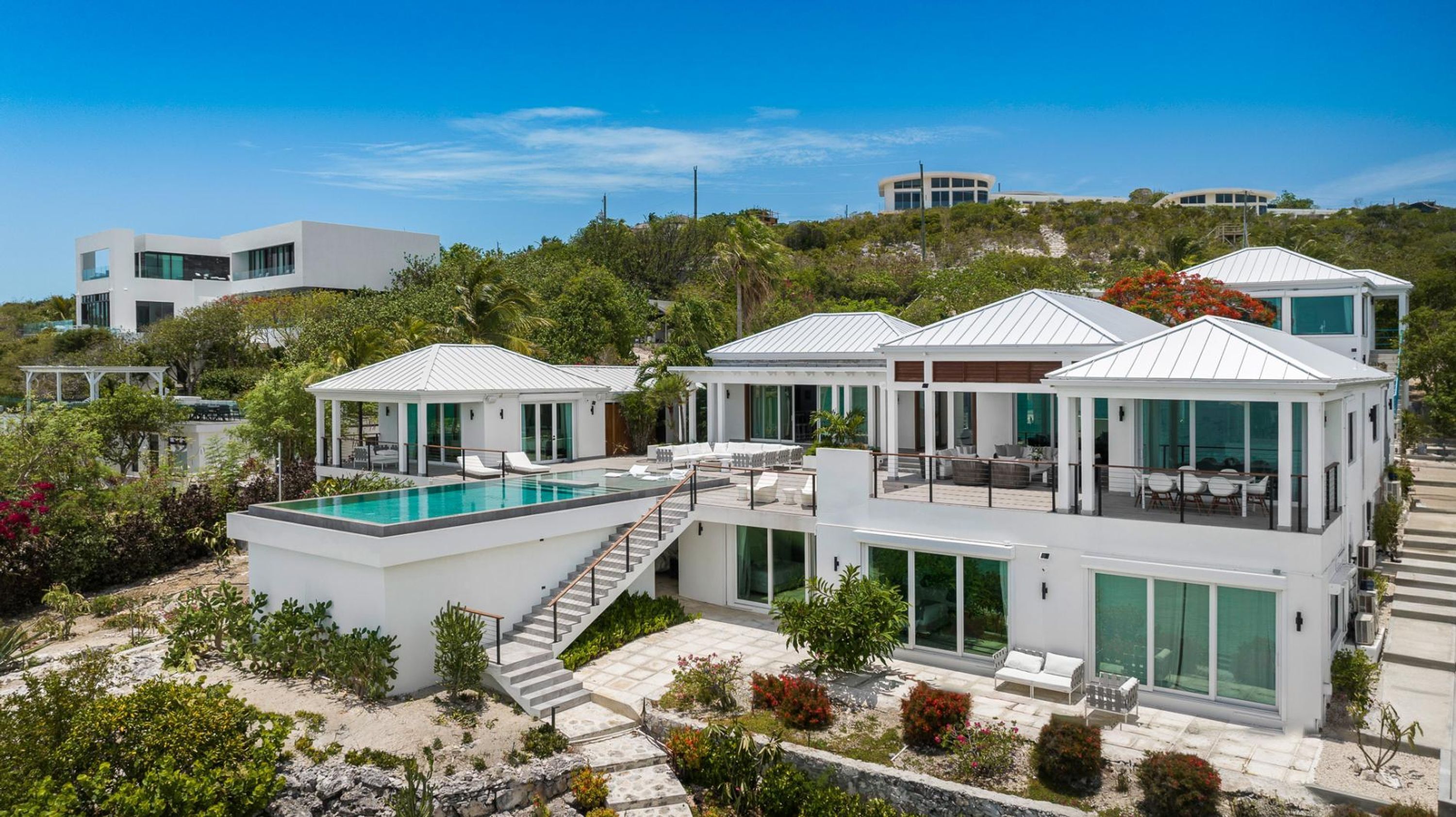 Eine moderne Villa mit Swimmingpool, mehreren Sitzbereichen im Freien und Blick auf die umliegende Landschaft.