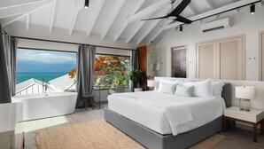 A modern bedroom with a large bed, a ceiling fan, a view of the ocean, and a bathtub. - Villa Eden in Providenciales (Providenciales)