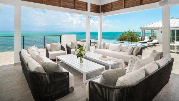 A spacious outdoor lounge area with a view of the ocean, featuring a white coffee table, sofas, and a dining table. - Villa Eden in Providenciales (Providenciales)