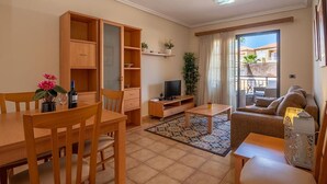 A living room with a dining table, chairs, a sofa, a TV, and a balcony with a view. - Apartamento Vanessa in Costa Adeje (Adeje)