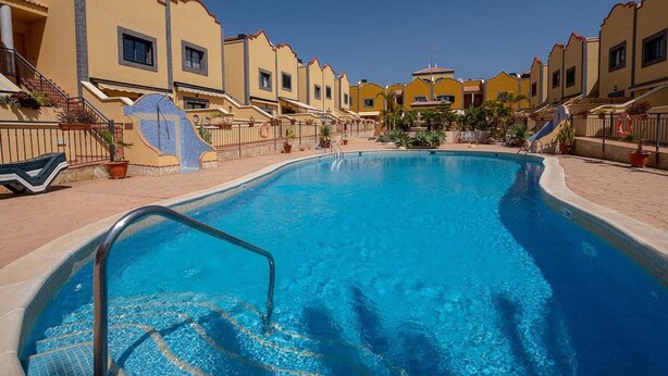 A swimming pool surrounded by yellow buildings with a clear blue sky. - Apartamento Vanessa in Costa Adeje (Adeje)