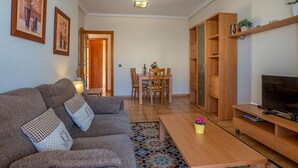 A living room with a sofa, coffee table, TV stand, and dining area. - Apartamento Vanessa in Costa Adeje (Adeje)