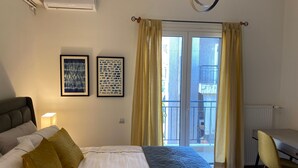 A bedroom with a bed, a desk, a chair, two framed artworks, a window with curtains, and an air conditioning unit. - Spacious Glyfada Golf 4BR -near Beach Shops (Glyfada)