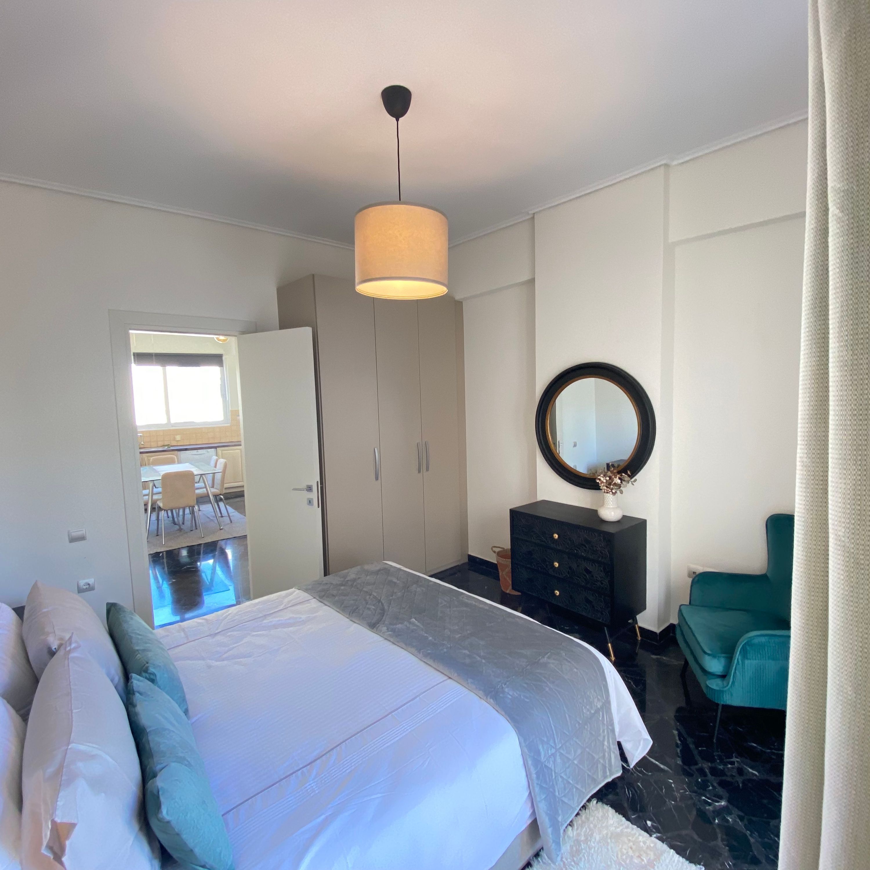 A bedroom with a bed, a dresser, a mirror, and a view of a dining area.