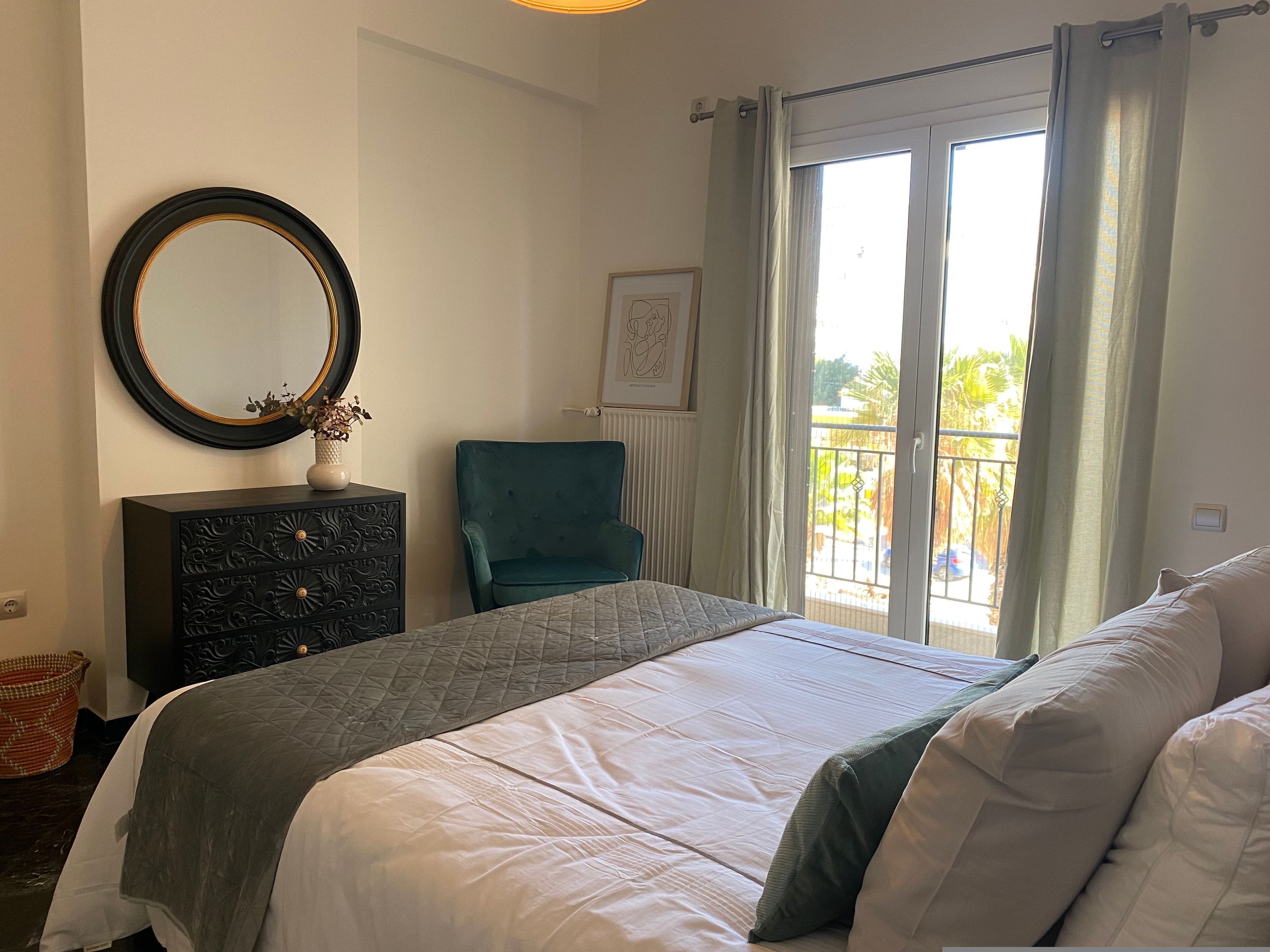 A bedroom with a bed, a dresser, a chair, a window with curtains, and a balcony view.