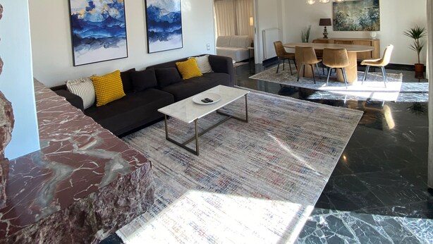A modern living room with a black sofa, a marble coffee table, and a dining area with a wooden table and chairs. - Spacious Glyfada Golf 4BR -near Beach Shops (Glyfada)