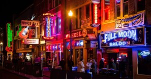 A vibrant street scene with neon signs for various establishments, including a music venue and a bar.