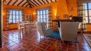 Une pièce spacieuse avec un sol carrelé, une cheminée, un coin repas avec des chaises et de grandes fenêtres avec des rideaux.