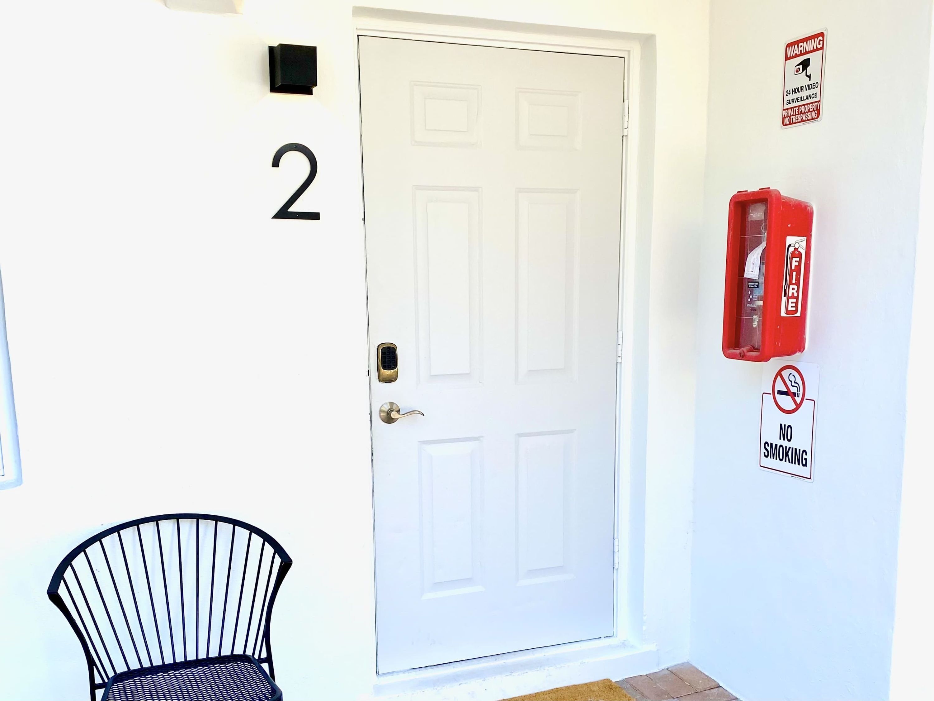 Una porta blanca amb el número 2 a la part superior, un extintor de foc muntat a la paret i un cartell de 'No Smoking'.