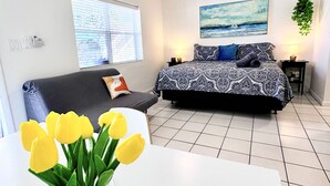 A bedroom with a bed, a sofa, a window with blinds, a painting on the wall, and a plant hanging from the ceiling. - Southwinds 2 for 3 King Studio for 3 w Kitchen (Hollywood)