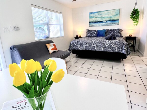 A bedroom with a bed, a sofa, a window with blinds, a painting on the wall, and a plant hanging from the ceiling. - Southwinds 2 for 3 King Studio for 3 w Kitchen (Hollywood)