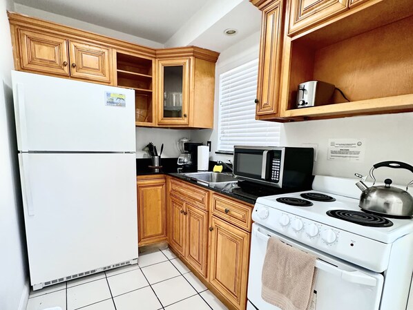 A kitchen with wooden cabinets, a white refrigerator, a microwave, a stove, and a sink.