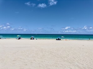 A beach with clear skies, calm waters, and a few umbrellas and lounge chairs.