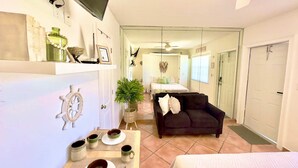 A well-lit, modern hotel room with a large bed, a dark sofa, a dining area with a table set for two, and a hallway leading to a bathroom. - Beach Lover s Studio Apartment in Hollywood FL (Hollywood)