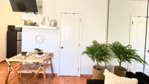 A compact living space with a kitchenette, a dining area with a table and chairs, a flat-screen TV mounted above the counter, and a large mirror reflecting the room. - Beach Lover s Studio Apartment in Hollywood FL (Hollywood)