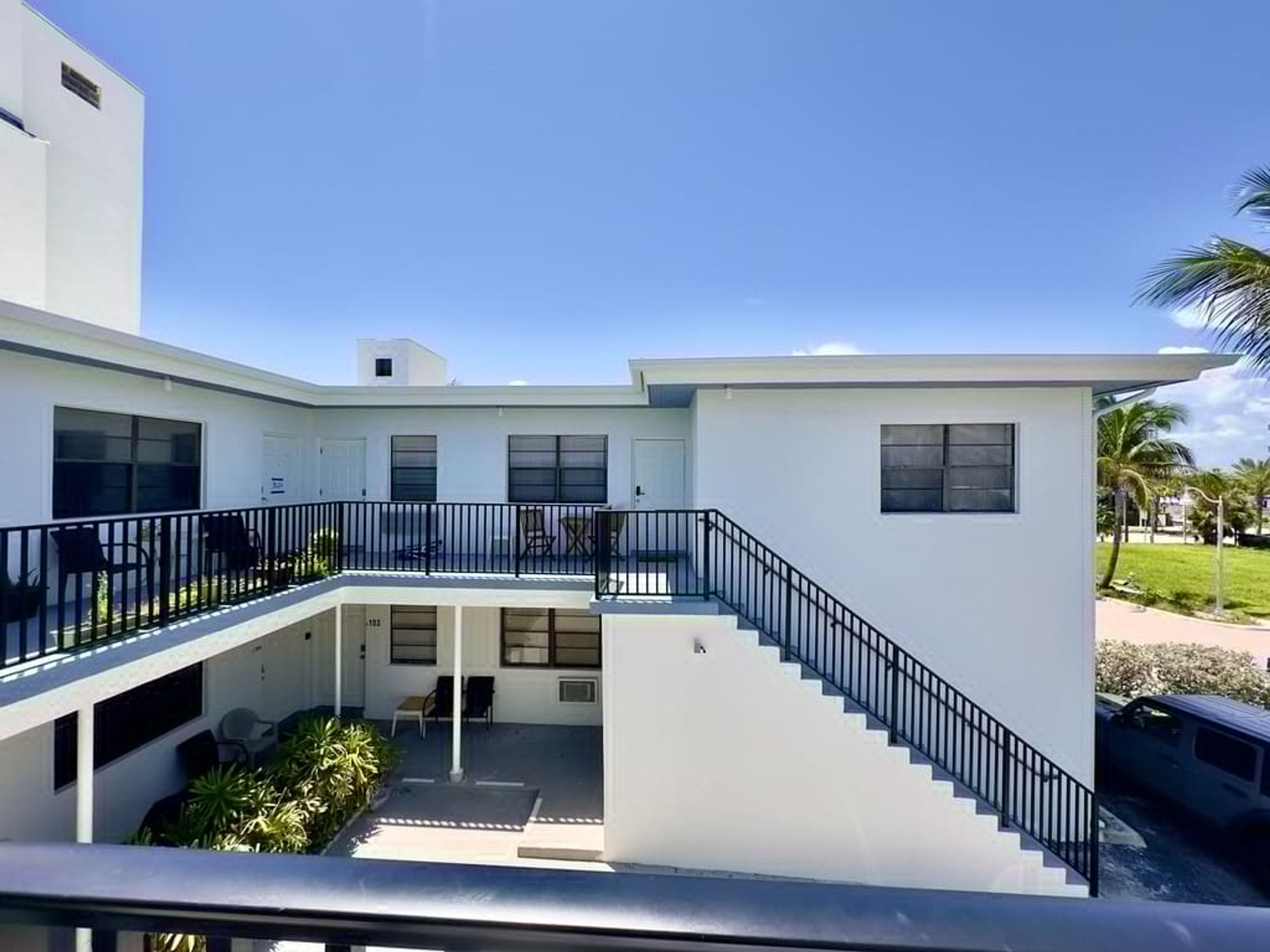 A modern two-story building with a covered outdoor area, a staircase, and a view of the surrounding greenery.