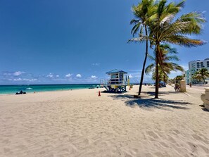 Une plage avec une tour de surveillance pour les sauveteurs, des palmiers et un ciel bleu dégagé.