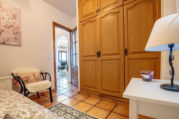 A room with a bed, a chair, a table with a lamp, and wooden wardrobes.