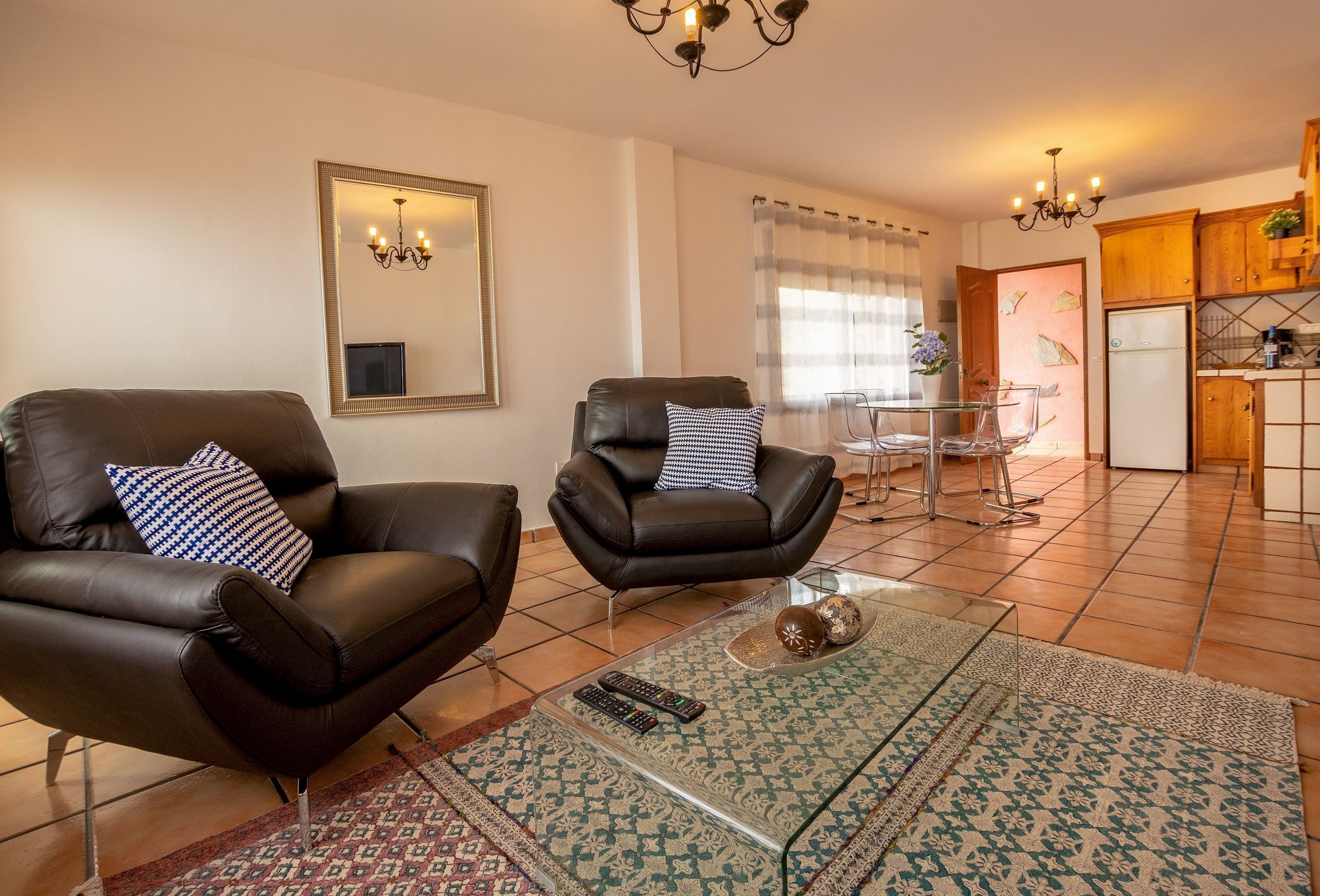 Una sala de estar con dos sillones de cuero, una mesa de centro de vidrio y un comedor con mesa y sillas de vidrio.