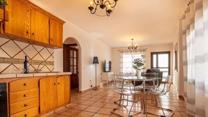 A kitchen with wooden cabinets, a tiled floor, and a dining area with a table and chairs. - Apartamento Lava in Adeje (Adeje)