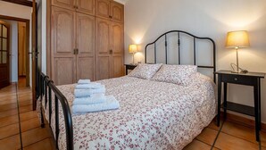 A bedroom with a bed, two bedside lamps, a wooden wardrobe, and a small table with a lamp. - Apartamento Lava in Adeje (Adeje)
