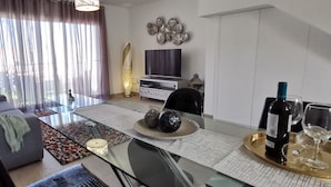 A modern living room with a sofa, a glass coffee table, a TV, and a dining area with a tray. - Villa Hortensia in Adeje (Adeje)