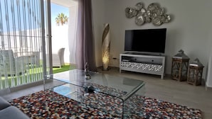 A modern living room with a glass coffee table, a sofa, and a TV on a white cabinet. - Villa Hortensia in Adeje (Adeje)