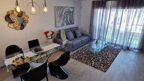 A modern living room with a glass dining table, black chairs, a grey sofa, a patterned rug, and a large abstract painting on the wall. - Villa Hortensia in Adeje (Adeje)